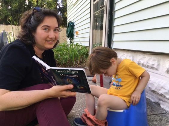 Em reading a book to Myron who is sitting on his potty outside our house